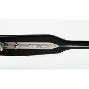 Close-up of the inner side of a black sunglasses frame showing the brand name 'JMM' and 'MADE IN THE JAPAN' printed on the acetate, with a silver metal hinge.