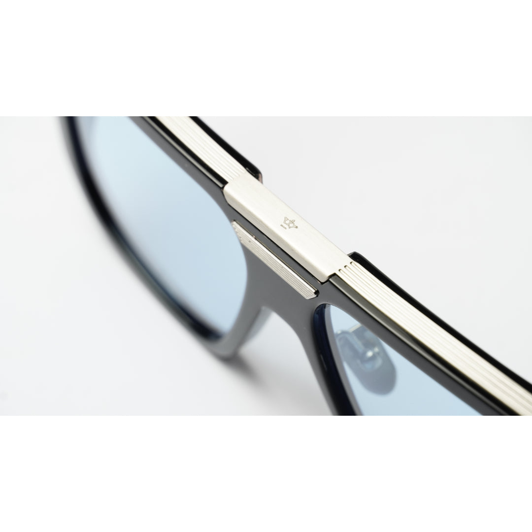 Close-up of a pair of eyeglasses showing a thick silver metal bridge and rim with light blue tinted lenses on a white background.