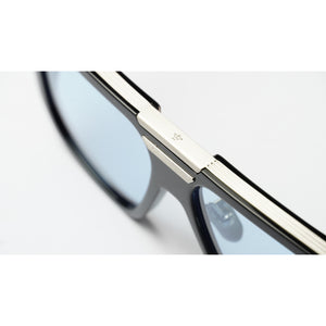 Close-up of a pair of eyeglasses showing a thick silver metal bridge and rim with light blue tinted lenses on a white background.