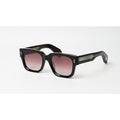 Black square sunglasses with gradient pink-tinted lenses and small gold geometric logo details on the temples, shown on a white background.
