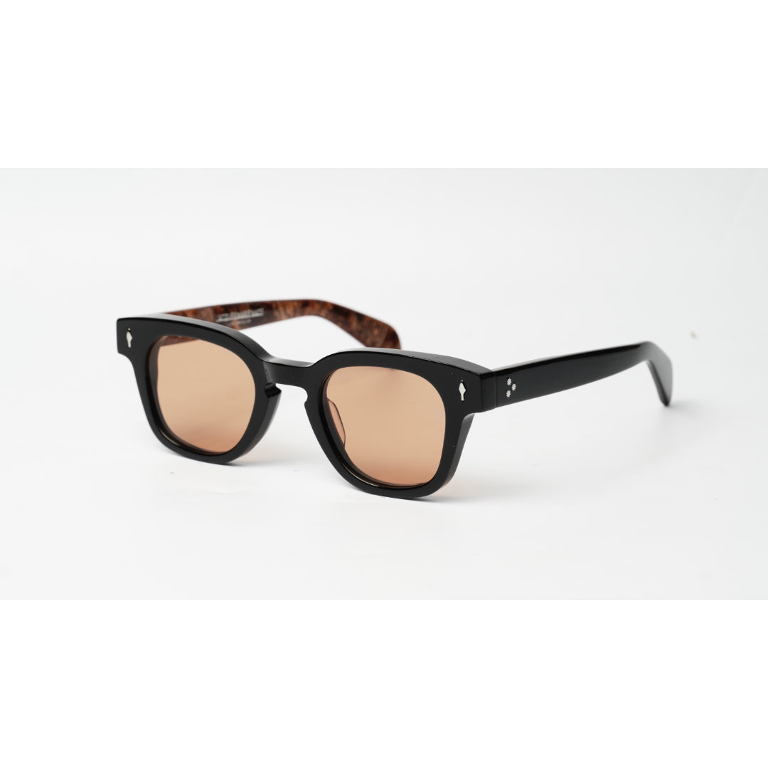 A pair of Jacques Marie Mage square-frame sunglasses with thick black frames, warm brown-tinted lenses, and tortoiseshell-patterned inner temples, shown on a clean white background.