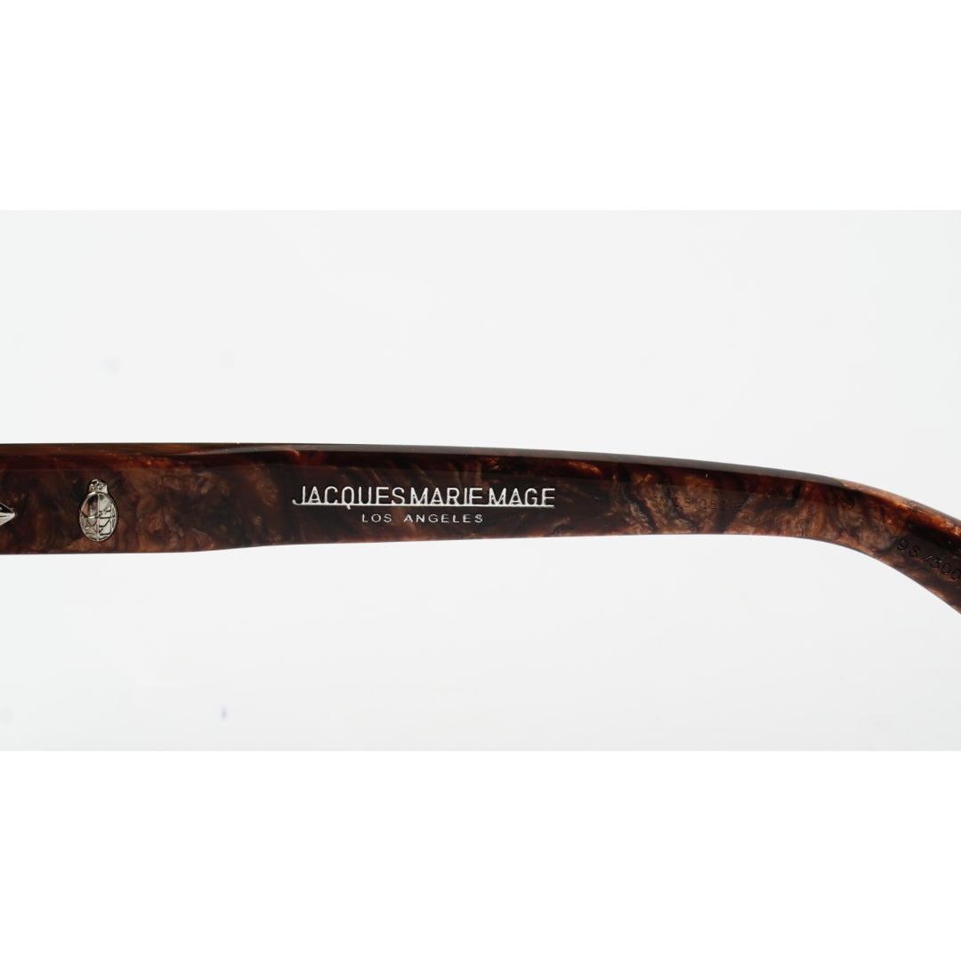 Close-up of a dark brown acetate eyeglass arm with a marbled pattern, featuring the brand name 'JACQUES MARIE MAGE LOS ANGELES' printed in silver lettering and a small silver decorative emblem.