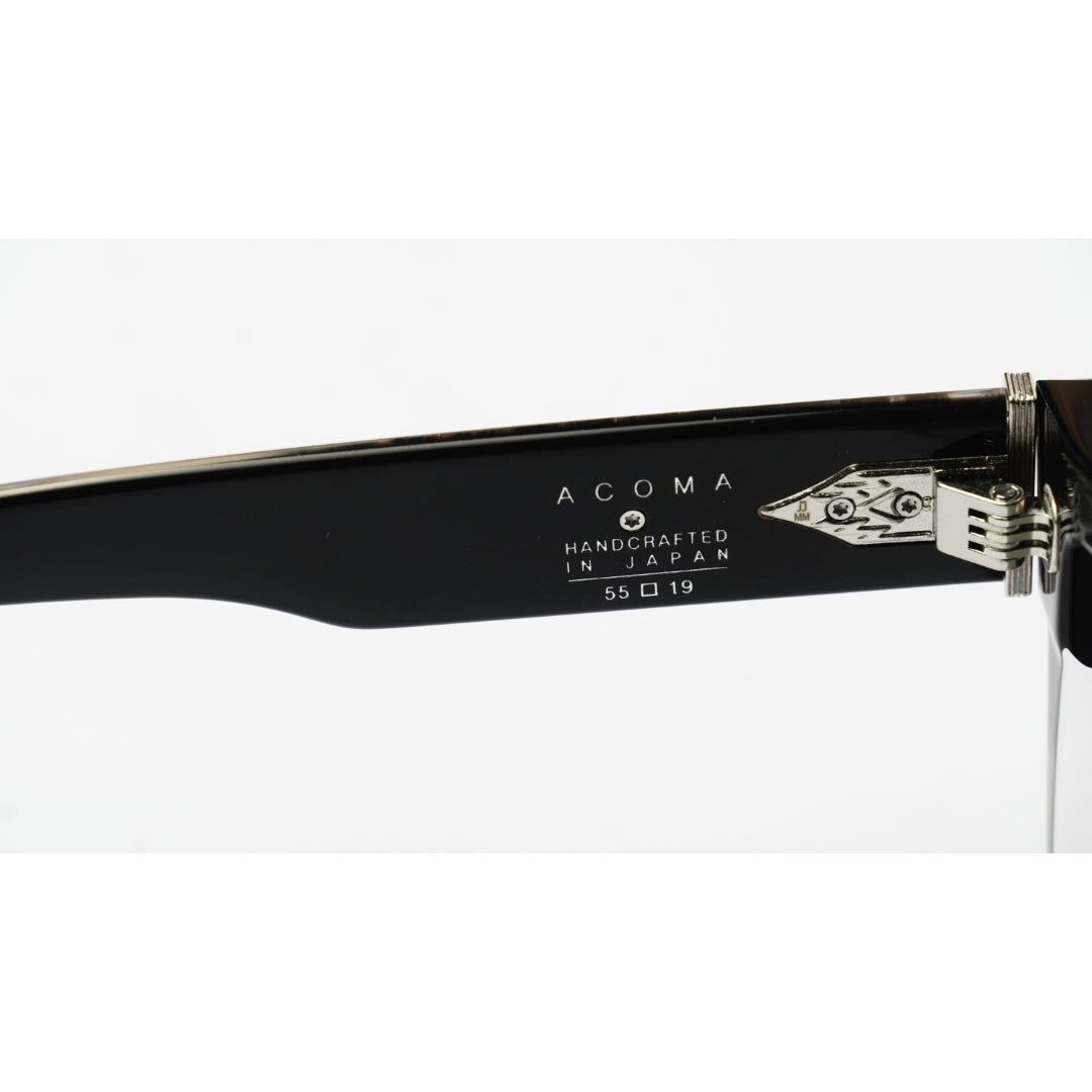 Close-up of the temple arm of Acoma eyeglasses, showing the black acetate frame, silver hinge, and white printed text 'ACOMA HANDCRAFTED IN JAPAN 55 □ 19' on a white background.