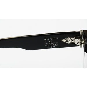 Close-up of the temple arm of Acoma eyeglasses, showing the black acetate frame, silver hinge, and white printed text 'ACOMA HANDCRAFTED IN JAPAN 55 □ 19' on a white background.