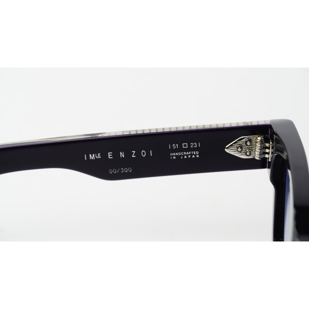 Close-up of the inner temple arm of a pair of black sunglasses, showing the brand name 'IMIZ ENZO and 'HANDICRAFTED IN JAPAN' alongside a silver metal hinge.