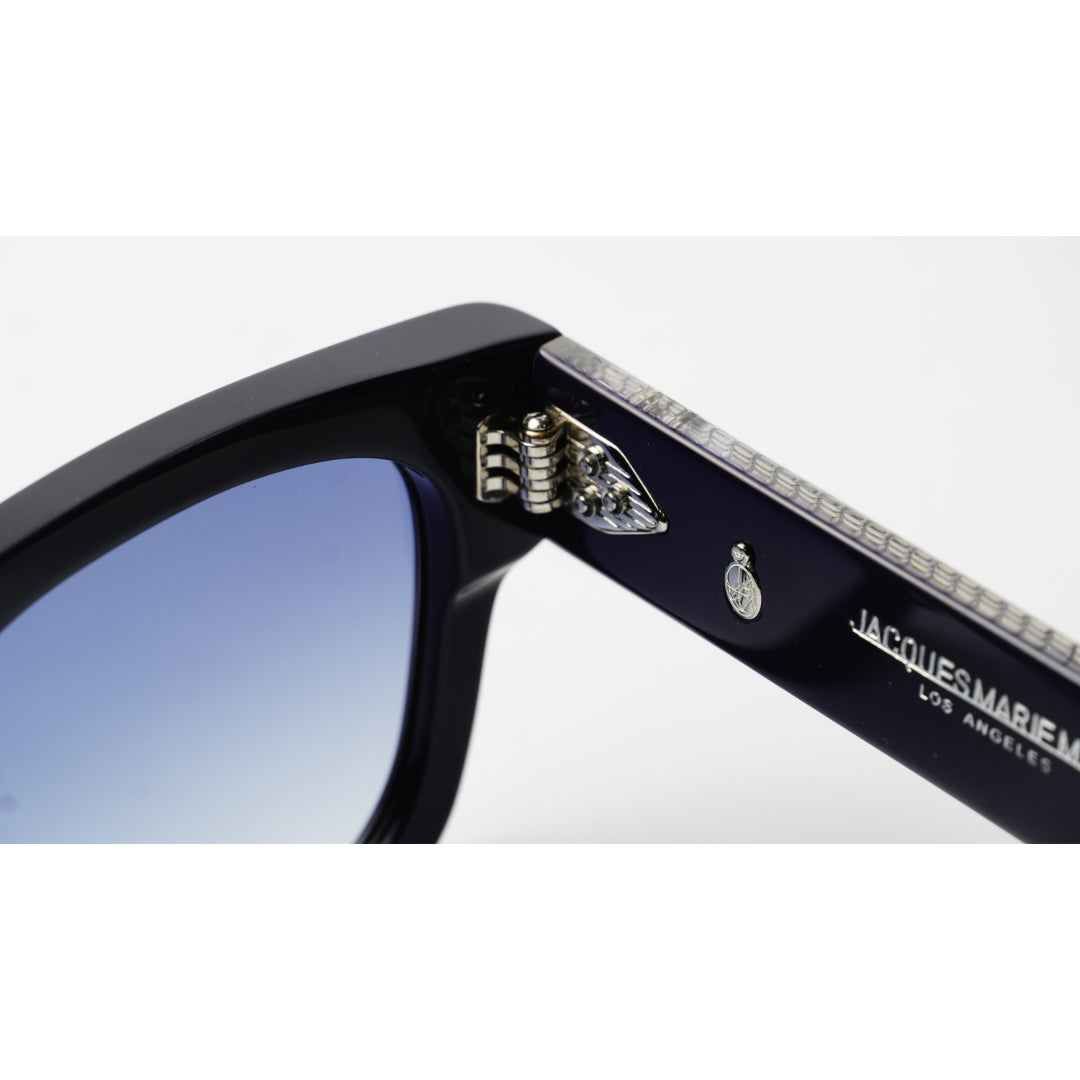 Close-up of a pair of Jacques Marier sunglasses showing the temple arm with rhinestone detailing, a silver hinge, and a blue-tinted lens against a white background.