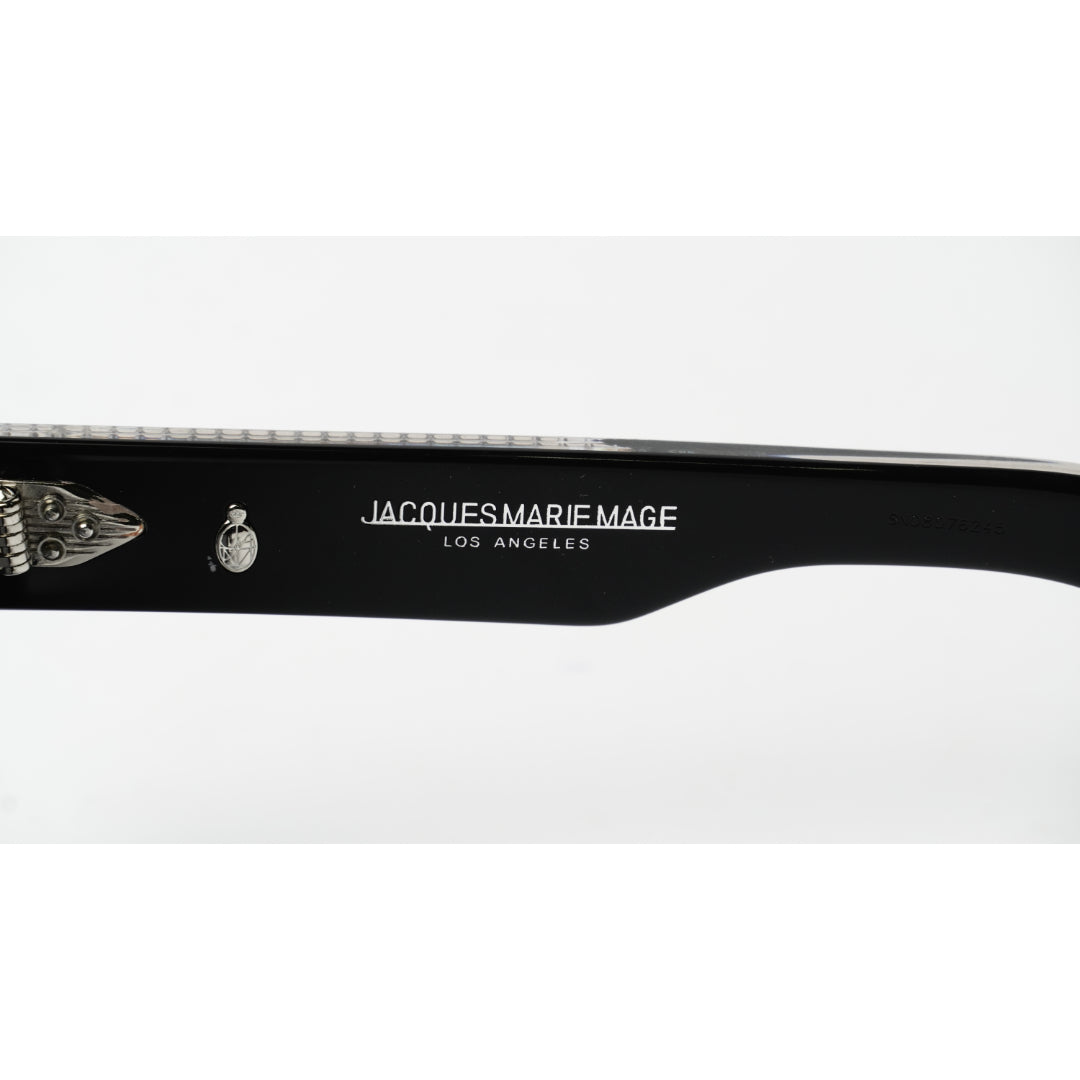 Close-up of a black sunglasses arm featuring white printed text that reads 'JACQUES MARIE MAGE LOS ANGELES' alongside a small skull-and-crossbones emblem, on a white background.
