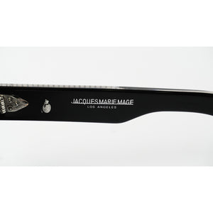 Close-up of a black sunglasses arm featuring white printed text that reads 'JACQUES MARIE MAGE LOS ANGELES' alongside a small skull-and-crossbones emblem, on a white background.