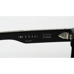 Close-up of the inner temple arm of black sunglasses, showing the brand name 'IM ENZO' and model details '51 □ 231 HANDMADE IN JAPAN' in white text, alongside a silver metal hinge.