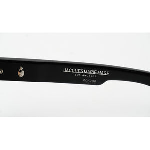 Close-up of a black acetate sunglasses arm with white printed text reading 'JACQUES MARIE MAGE LOS ANGELES 60/200' and a silver metal rivet on a white background.